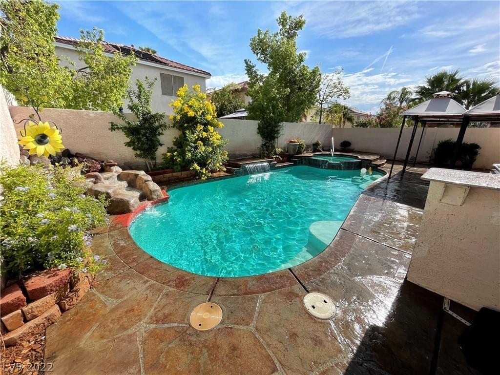 A cheerful outdoor area featuring a clear teal pool, stone patio, water feature, and landscaping